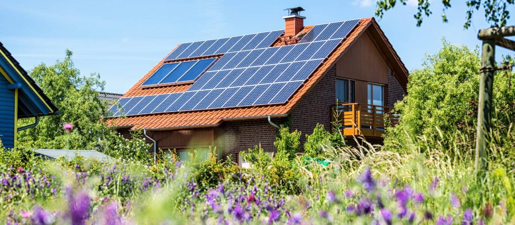 Haus mit Photovoltaikanlage und Blumen im Vordergrund | Klimaschutzgesetz Schleswig-Holstein