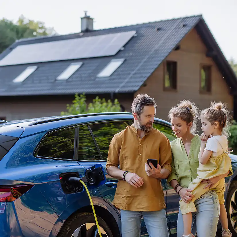 Familie vor einem Haus mit Photovoltaik und E-Mobilität.
